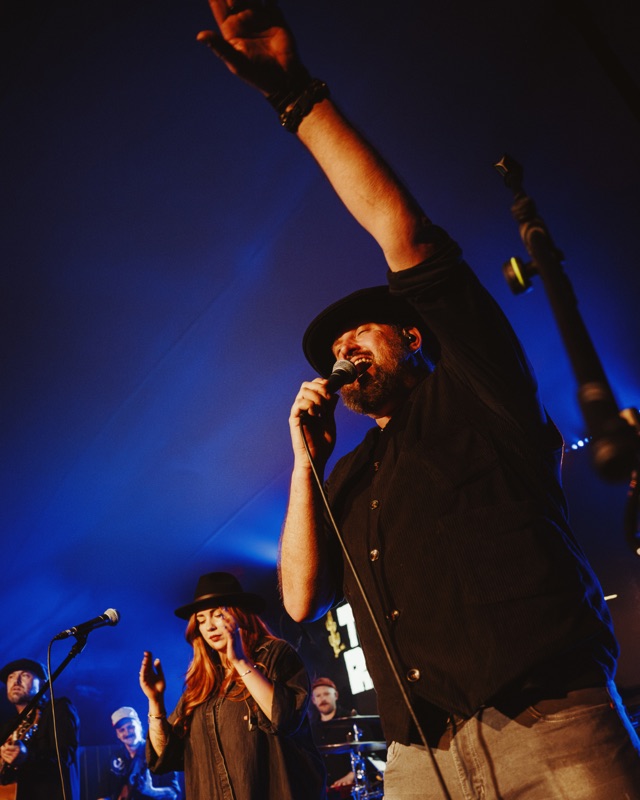 A lead vocalist with an arm raised, lit blue on a festival stage