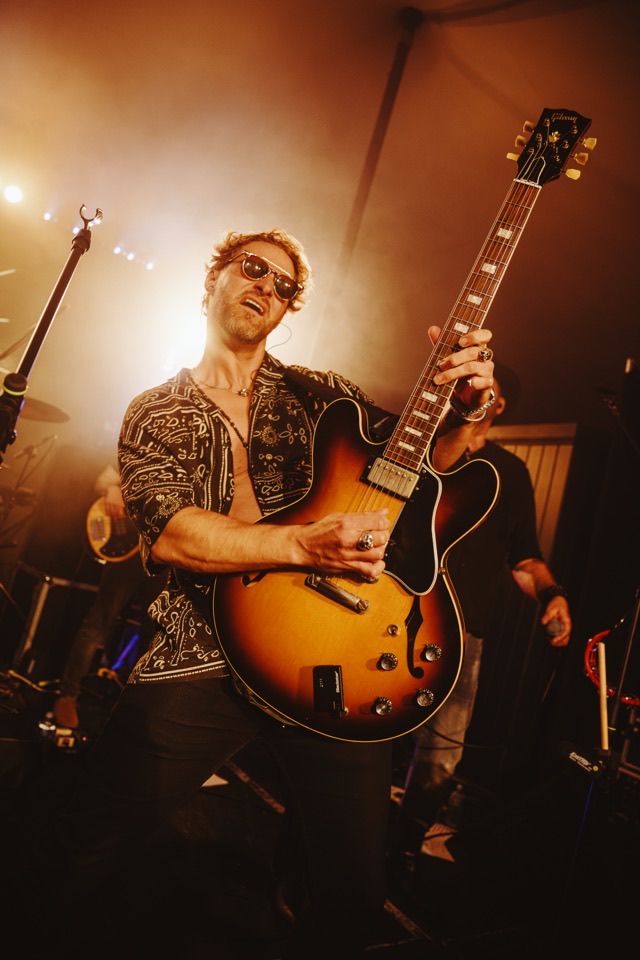 A guitarist playing a semi-acoustic under warm stage lights