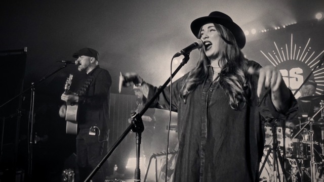 Two of the band singing together on stage, in monochrome